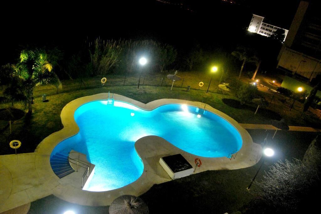 Una piscina de forma singular, rodeada por una terraza bien iluminada y una escalera de acceso.