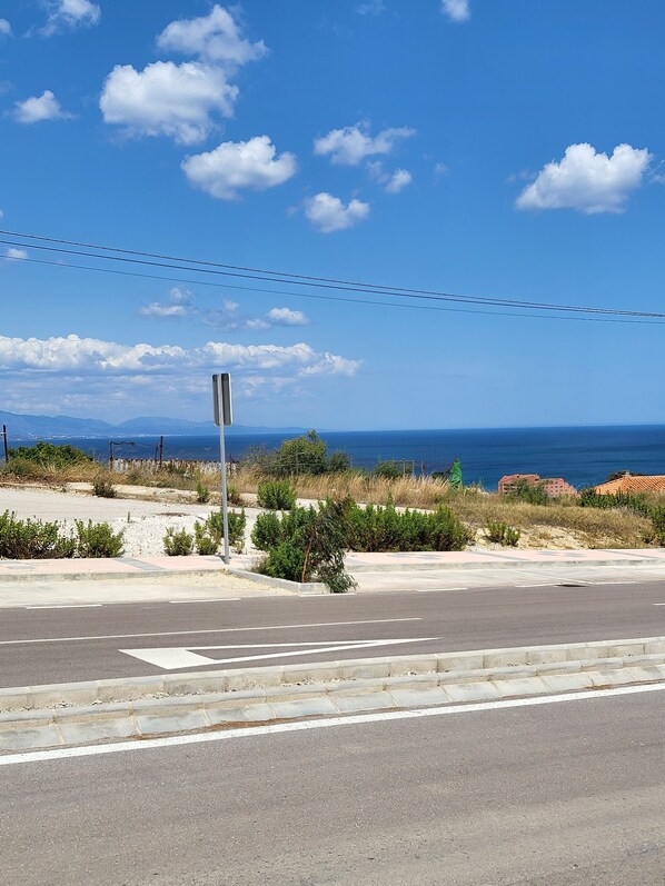 Eine Küstenstraße mit Zebrastreifen, einer Straßenlaterne und freiem Blick auf das Meer und entfernte Gebäude.