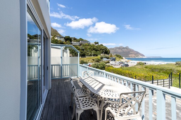 A balcony with a table and chairs, overlooking a coastal area with houses and a view of the ocean.