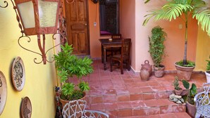 Um pátio com porta de madeira, mesa e cadeiras, e diversos vasos de plantas.