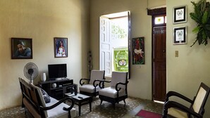 Uma sala de estar com televisão, duas poltronas, um sofá, um ventilador e uma porta que dá para o exterior.