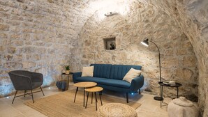 Een knus interieur met een stenen muur, een blauwe bank, een grijze fauteuil en een tafeltje met een lamp.