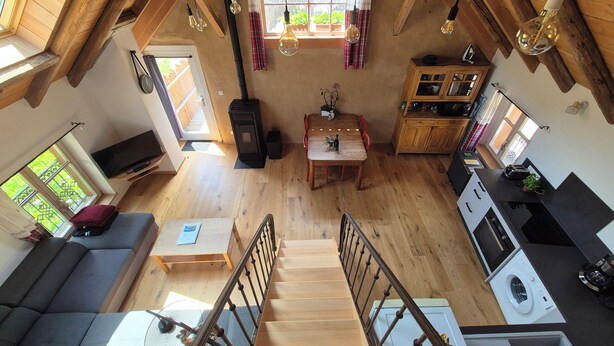Un vaste espace de vie de style loft, comprenant un escalier en bois, un coin repas, une cuisine et un salon avec un canapé et une table.