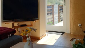 Un salon chaleureux doté d’un téléviseur à écran plat, d’un plafond en bois et offrant une vue sur un balcon agrémenté d’une barrière en bois.