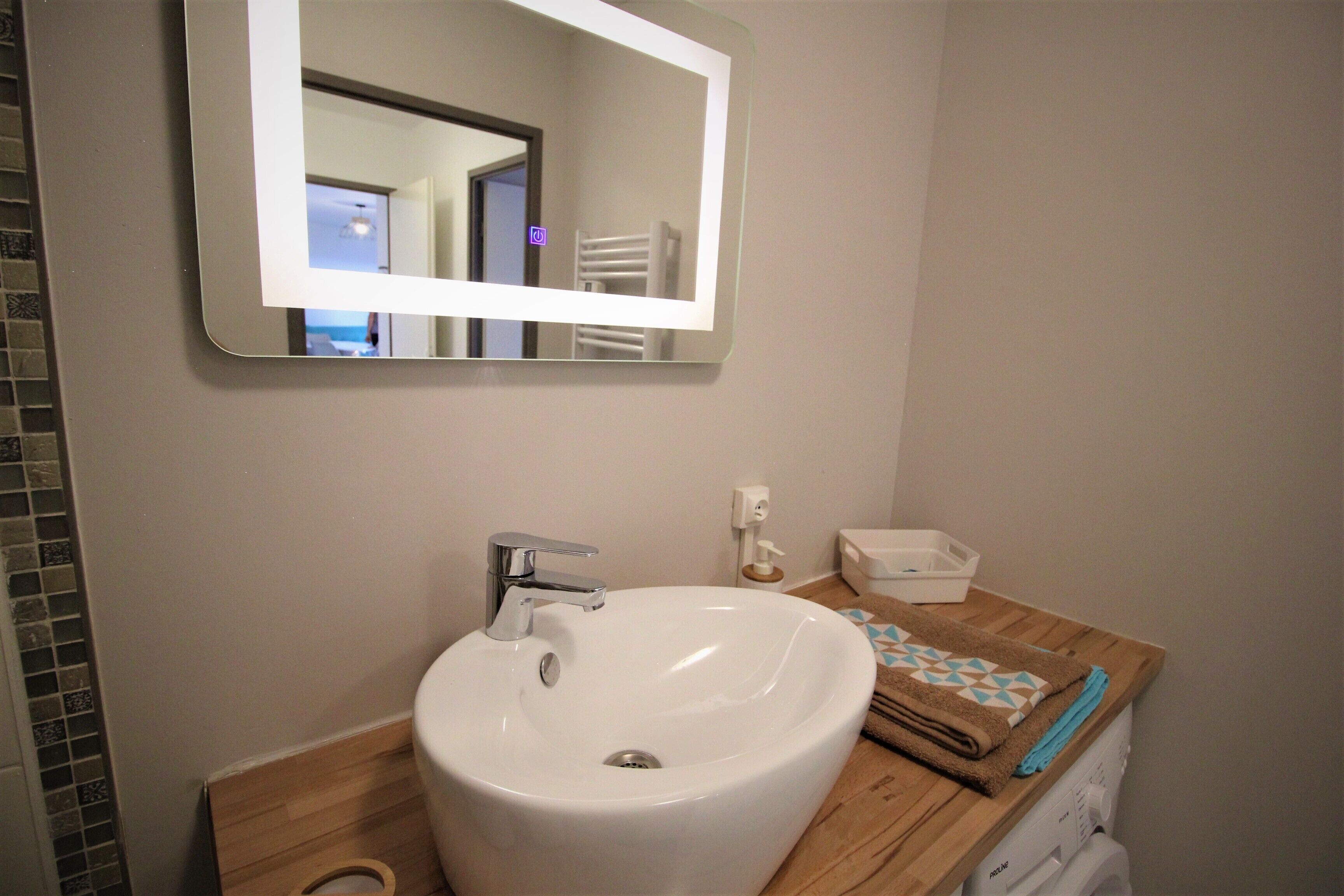 Une salle de bain avec un lavabo blanc, un miroir, un porte-serviettes et un meuble-lavabo en bois.
