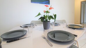 Una mesa de comedor lista con platos, cubiertos y vasos, con una planta en maceta y un cuadro en la pared.