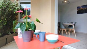 Una mesa naranja brillante con una planta en maceta, un florero blanco y una taza azul.
