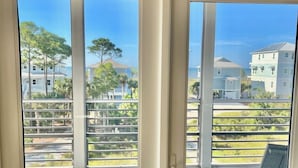 Een balkon met uitzicht op zee en gebouwen, een plafondventilator en een deur met een handvat.