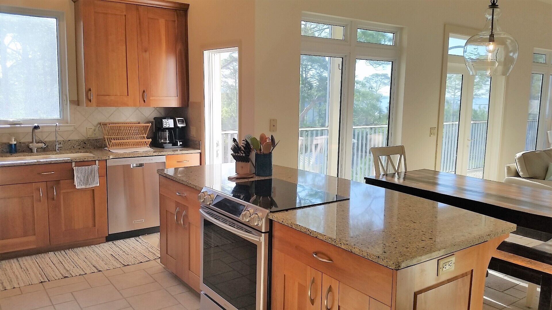 A kitchen with wooden cabinets, a stainless steel oven, a granite countertop, and a dining area with a chair.
