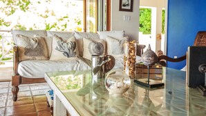 Ein Wohnzimmer mit einem Glastisch, einer Couch mit dekorativen Kissen und Blick ins Grüne.