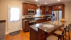 A modern kitchen with wooden cabinets, stainless steel appliances, and a granite countertop. - Spacious 4-BR Home – Open Concept, Deck & Parking! (Pittsburgh)
