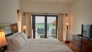 A hotel room with a bed, a TV, a dresser, and a view of the beach through the door.