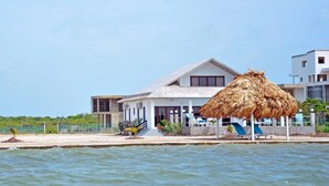 A beachfront property with a thatched-roof structure, a pool, and a white building with a grey roof.