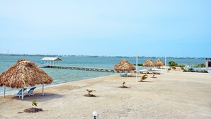 A beach with thatched umbrellas, lounge chairs, and a pier extending into the water.