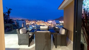 A balcony with wicker furniture and a view of a cityscape at dusk.
