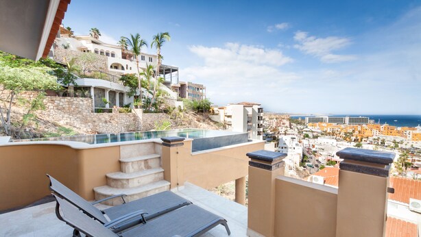 A balcony with a pool, steps leading up to a house, and a view of the city and sea.