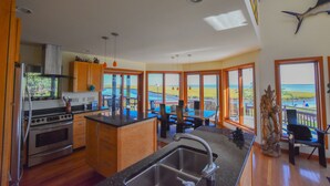 Eine moderne Küche mit einer großen Kochinsel, Holzschränken und Meerblick durch große Fenster.