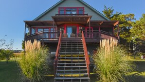 Ein zweistöckiges Haus mit einer Veranda, einer Treppe, die zum Eingang führt, und einem gepflegten Rasen.
