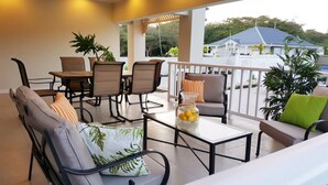 A covered outdoor seating area with chairs and tables, a view of a house in the background, and potted plants. - Flamingo Villa in quiet & secure gated development close to airport, beaches  (Canaan)