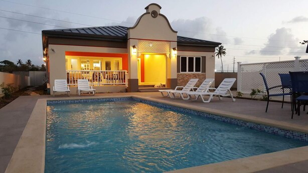 A poolside area with a swimming pool, lounge chairs, and a building with a covered patio. - Flamingo Villa in quiet & secure gated development close to airport, beaches  (Canaan)