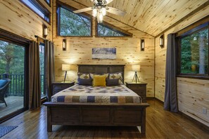 Un dormitorio de cabaña de madera con una cama grande, dos mesitas de noche y un ventilador de techo.