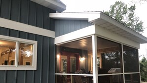 A house with a covered porch and a large windowed area. - Get back to nature and experience lake life in style when you stay at our house (Albion)