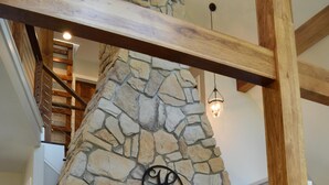 A stone fireplace with a wooden mantel, a hanging light fixture, and a staircase in the background. - Get back to nature and experience lake life in style when you stay at our house (Albion)