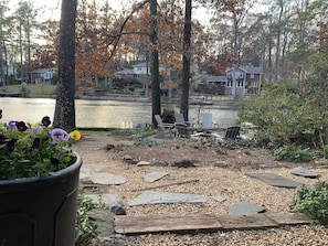 A lakeside patio with Adirondack chairs and a stone pathway leading to the water.