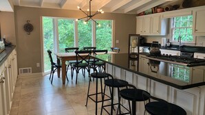 Een ruime keuken met een groot eiland, witte kasten en een eethoek met een houten tafel en stoelen.