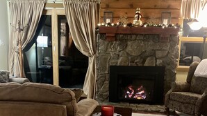 A cozy living room with a stone fireplace, a brown sofa, and a wicker basket on a wooden table. - Beautiful 3 BR ski In Trailside condo.  Steps away from WaterPark & Ice Rink  (Jay)