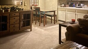 A cozy living room with a fireplace, a dining area with a chandelier, and a kitchen with white cabinets and a microwave. - Beautiful 3 BR ski In Trailside condo.  Steps away from WaterPark & Ice Rink  (Jay)