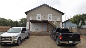 Two pickup trucks parked in front of a two-story building with a balcony and a staircase leading to the entrance.