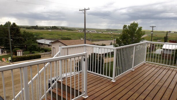 A wooden deck with white railings, overlooking a rural landscape with houses and fields.