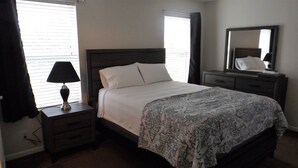 A neatly made bed with a patterned bedspread, a bedside lamp, and a nightstand with a drawer.