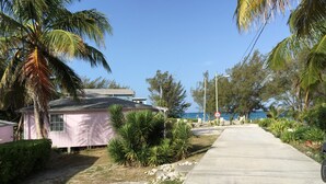 Une maison rose avec une allée pavée, des palmiers et un panneau de signalisation indiquant un arrêt.