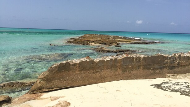 Une plage avec une eau turquoise et limpide, des formations rocheuses et un rivage sablonneux.