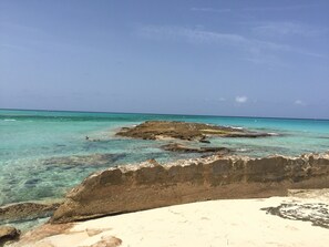 Una playa con agua turquesa cristalina, formaciones rocosas y un primer plano arenoso.
