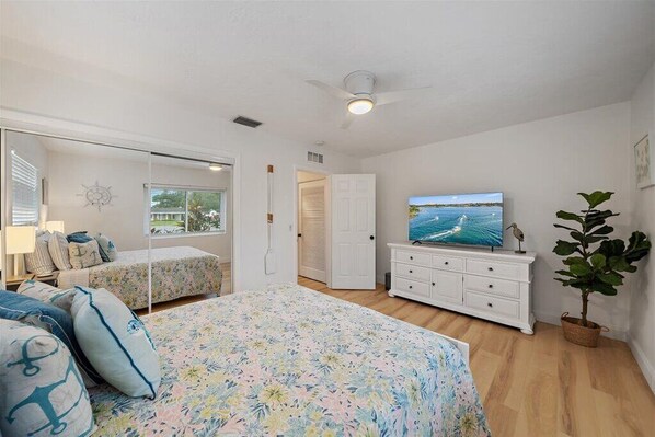 A bedroom with a bed, a dresser, a television, and a potted plant. - The Blue Conch – Family Friendly - Read About the 4th Bedroom - 3D Tour (Sarasota)