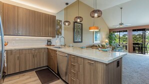 Een moderne keuken met houten kasten, een centraal eiland, hanglampen en uitzicht op de buitenruimte.