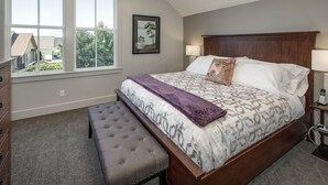 A bedroom with a large bed, a bench, a dresser, and a window with a view of buildings and trees. - La Conner, Tillinghast Residence E #401 (La Conner)