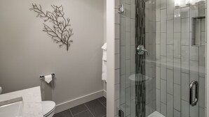 A modern bathroom with a glass shower enclosure, a marble sink, and a wall-mounted toilet. - La Conner, Tillinghast Residence E #401 (La Conner)