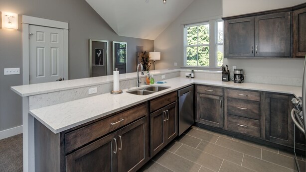 A modern kitchen with dark wood cabinets, a white countertop, and a large window providing natural light. - La Conner, Tillinghast Residence E #401 (La Conner)