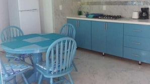 Cocina pequeña con armarios azules, un refrigerador blanco, un microondas y una estufa a gas. Hay una mesa redonda con sillas azules.