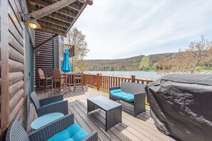 Een houten terras met rieten meubilair, een overdekte barbecue en uitzicht op een meer en heuvels.