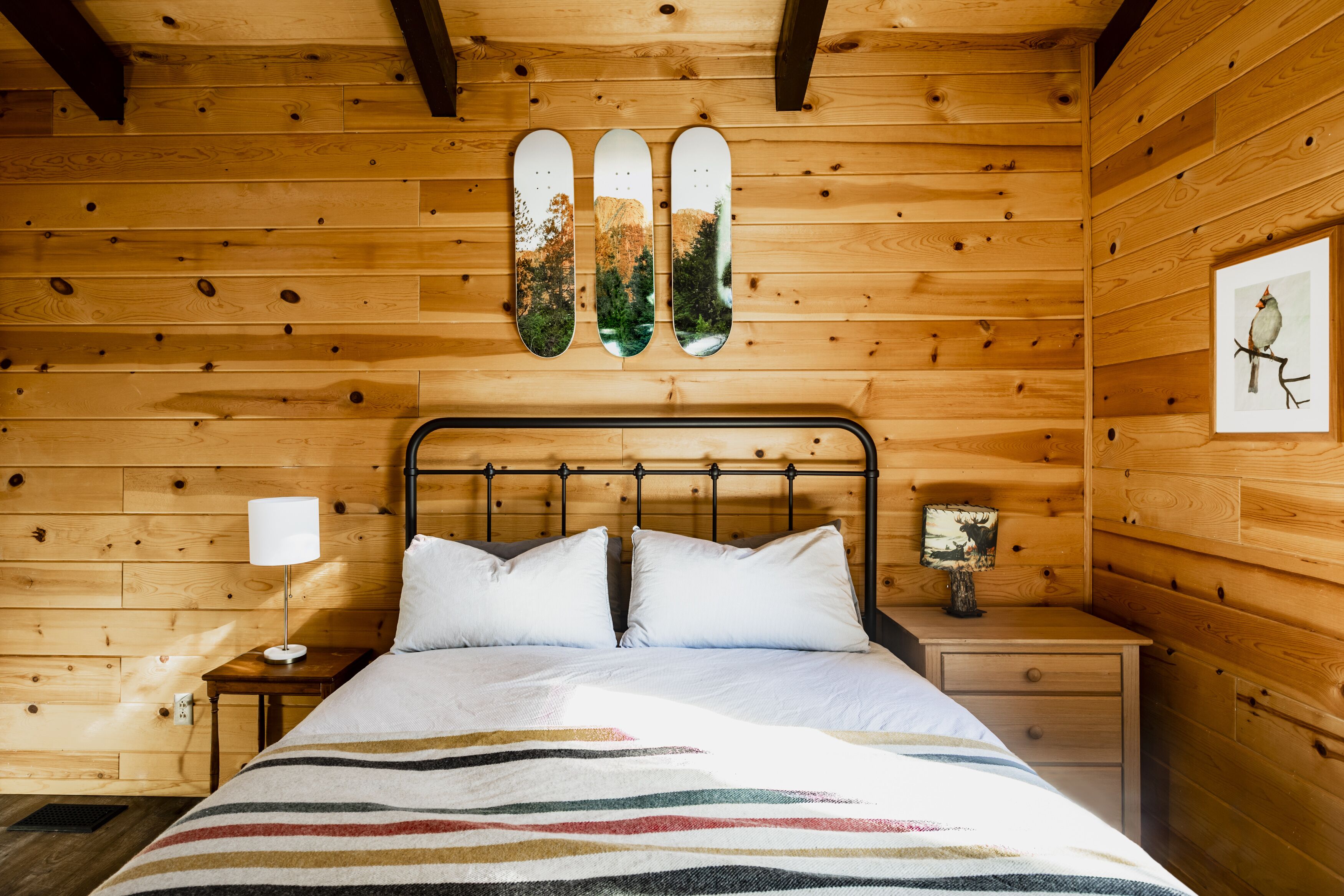A wooden cabin bedroom with a bed, a nightstand, a lamp, and a framed picture on the wall.