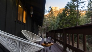 Una terraza de madera con dos sillas de mimbre blanco y una mesita con una botella y un vaso.