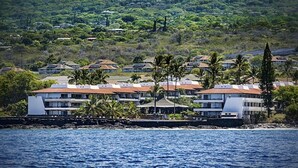 Un hôtel situé sur la côte, composé de plusieurs bâtiments, dont certains ont des toits rouges et d’autres des façades blanches, et qui se trouve à proximité d’une étendue d’eau.