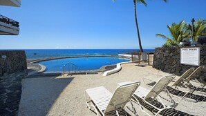 Un espace piscine équipé de chaises longues, d’un palmier et d’un panneau indiquant les règles à respecter.