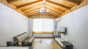 A room with a wooden ceiling, a sofa, a dining table, and a TV. - Kyung-po Stone Valley (Gangneung)