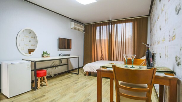 A compact hotel room with a bed, a desk with a computer, a small fridge, and a chair. - Kyung-po Stone Valley (Gangneung)